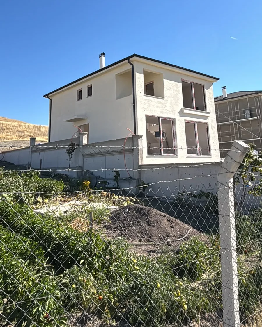 Çevre duvarının arkasında bacalı, cephesi tamamlanmış villa