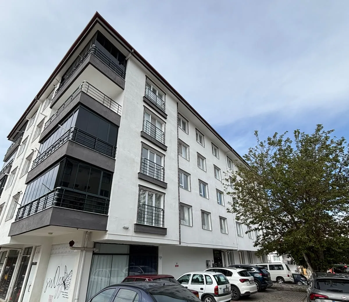 Antrasit balkon bantlı, beyaz cepheli, zemin katı dükkânlı beş katlı konut binasının köşeden görünümü