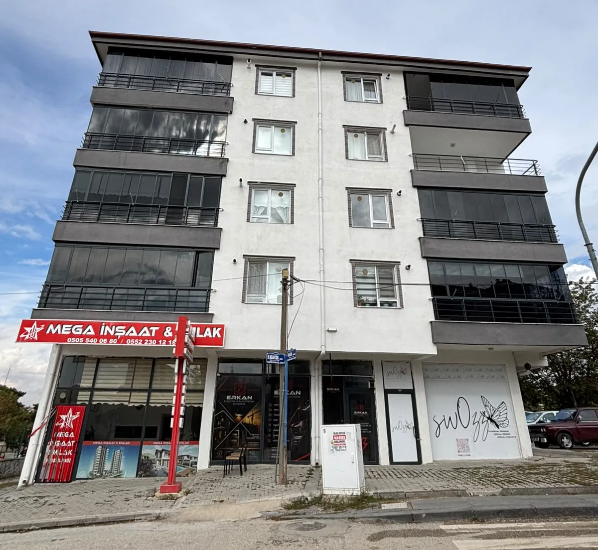 Konut binasının ön cephesi; zemin katta Mega İnşaat & Emlak tabelalı ofis ve yanındaki dükkânlar