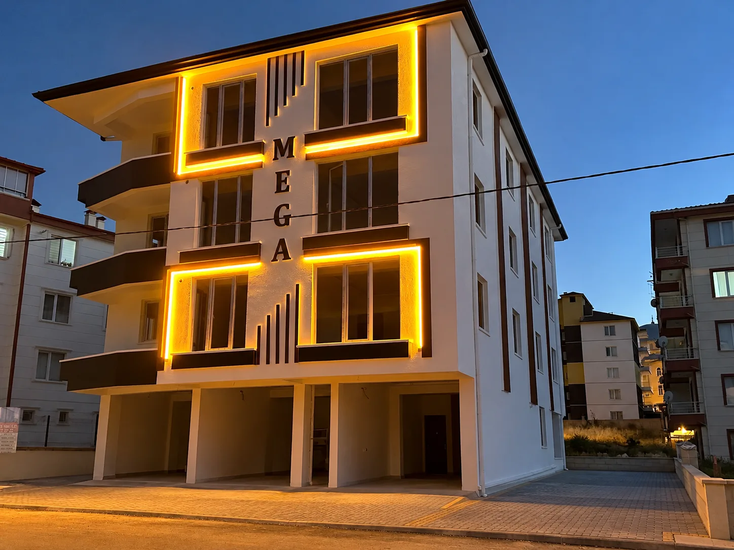 Işıklı pencere çerçeveleri, bordo dikey bantlı yan cephesi ve kilit taşı kaplı ön alanıyla konut binası