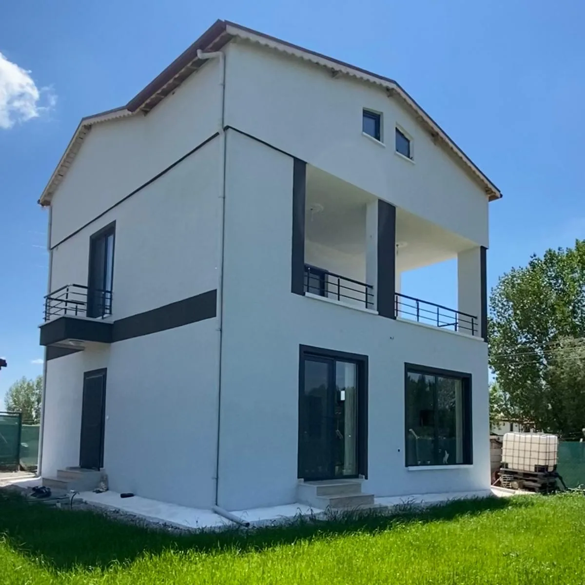 Çimenli bahçenin önünde beyaz cepheli, koyu çerçeveli doğramaları olan ev