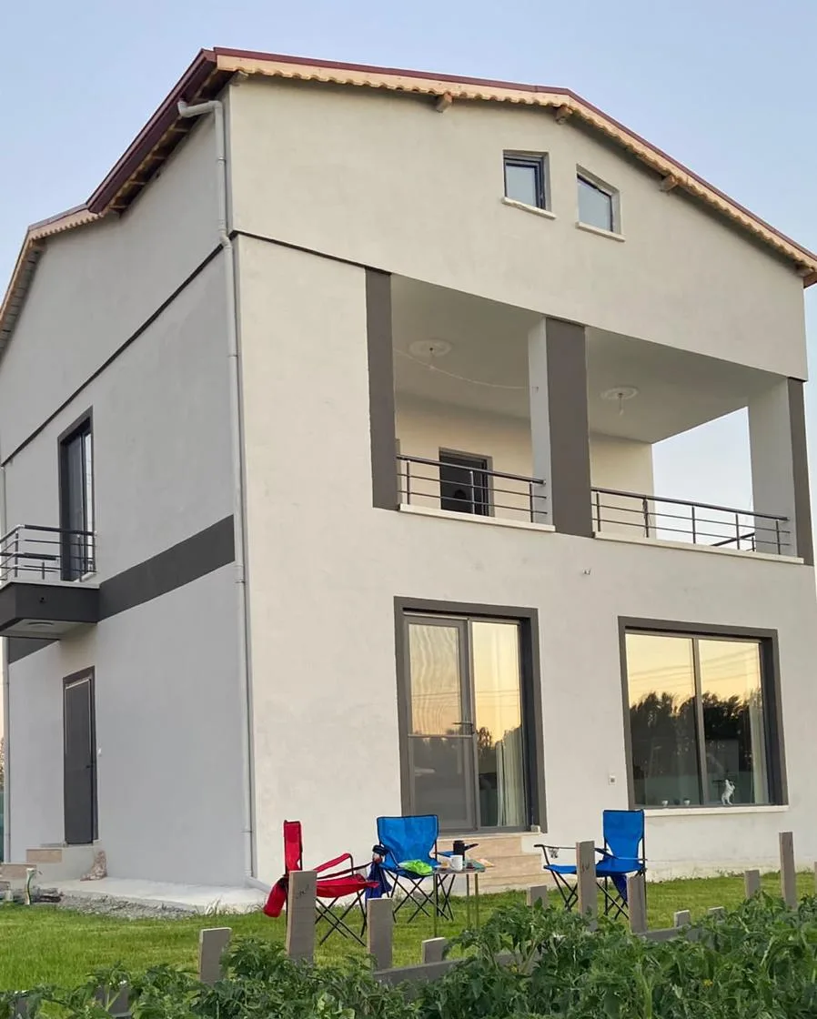 Gün batımında ev, bahçedeki kamp sandalyeleri ve önde domates fideleri