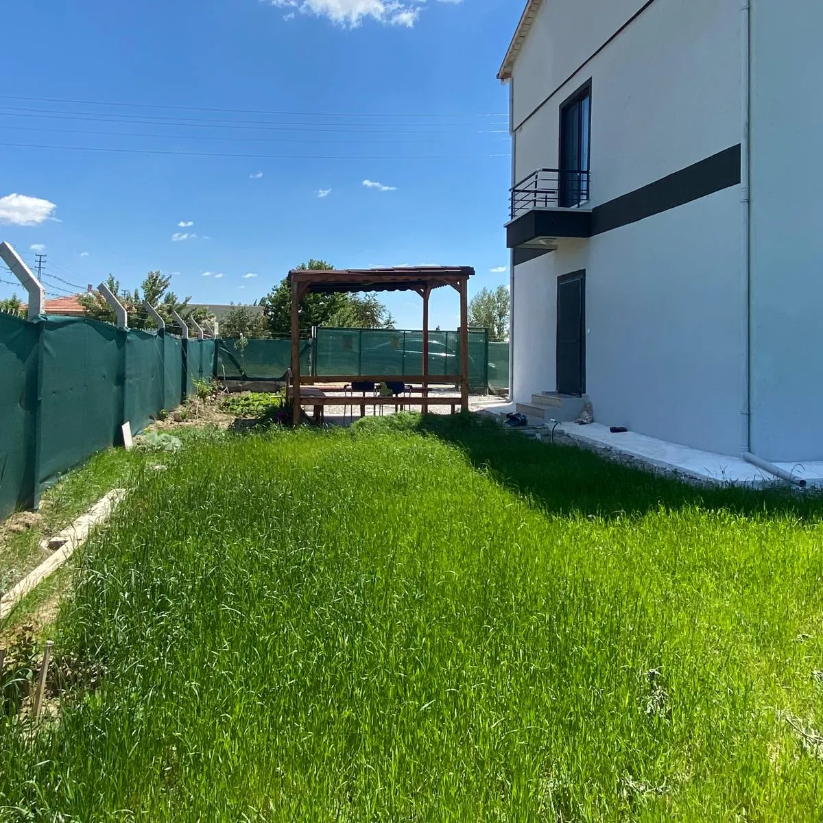 Evin yan cephesi, balkon ve bahçenin ucundaki ahşap kamelya